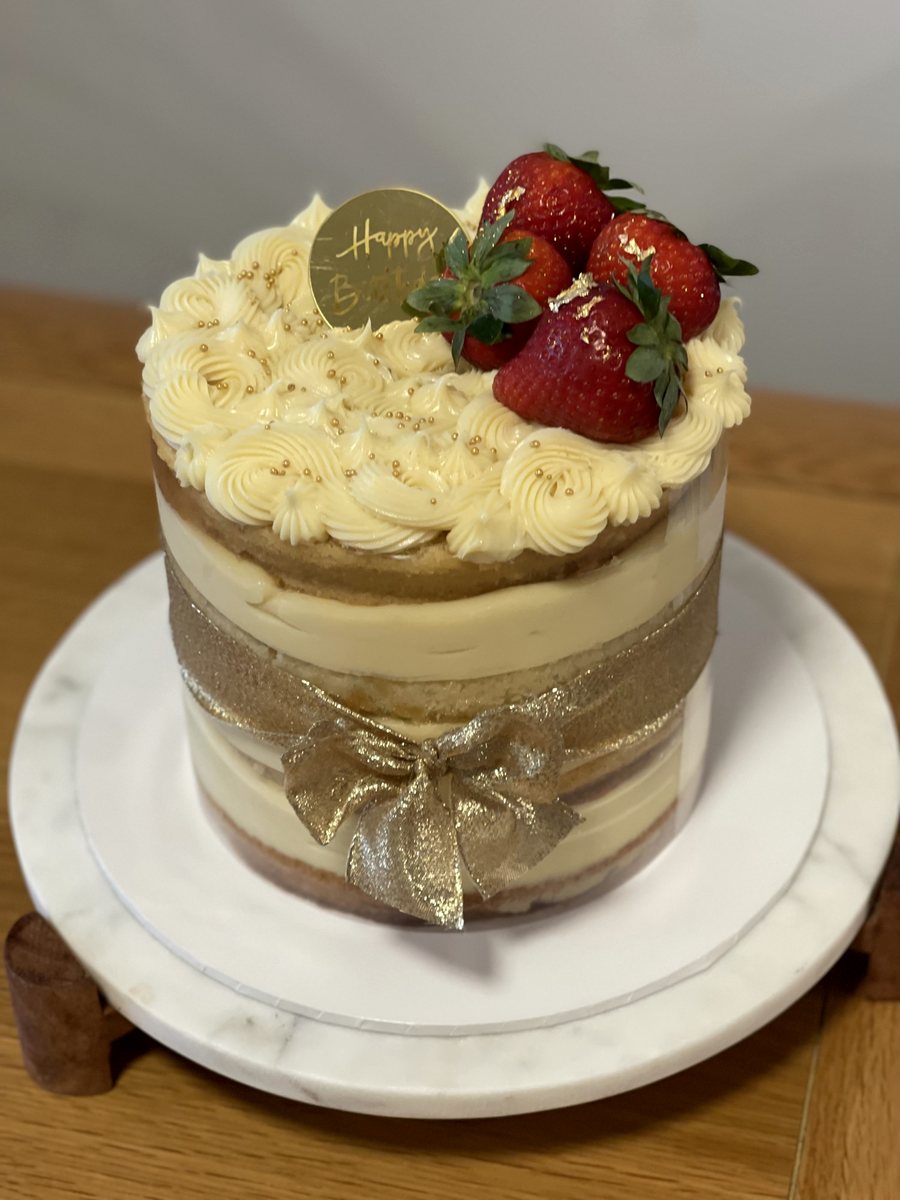 Naked cake with vanilla cream, fresh strawberries and a gold ribbon